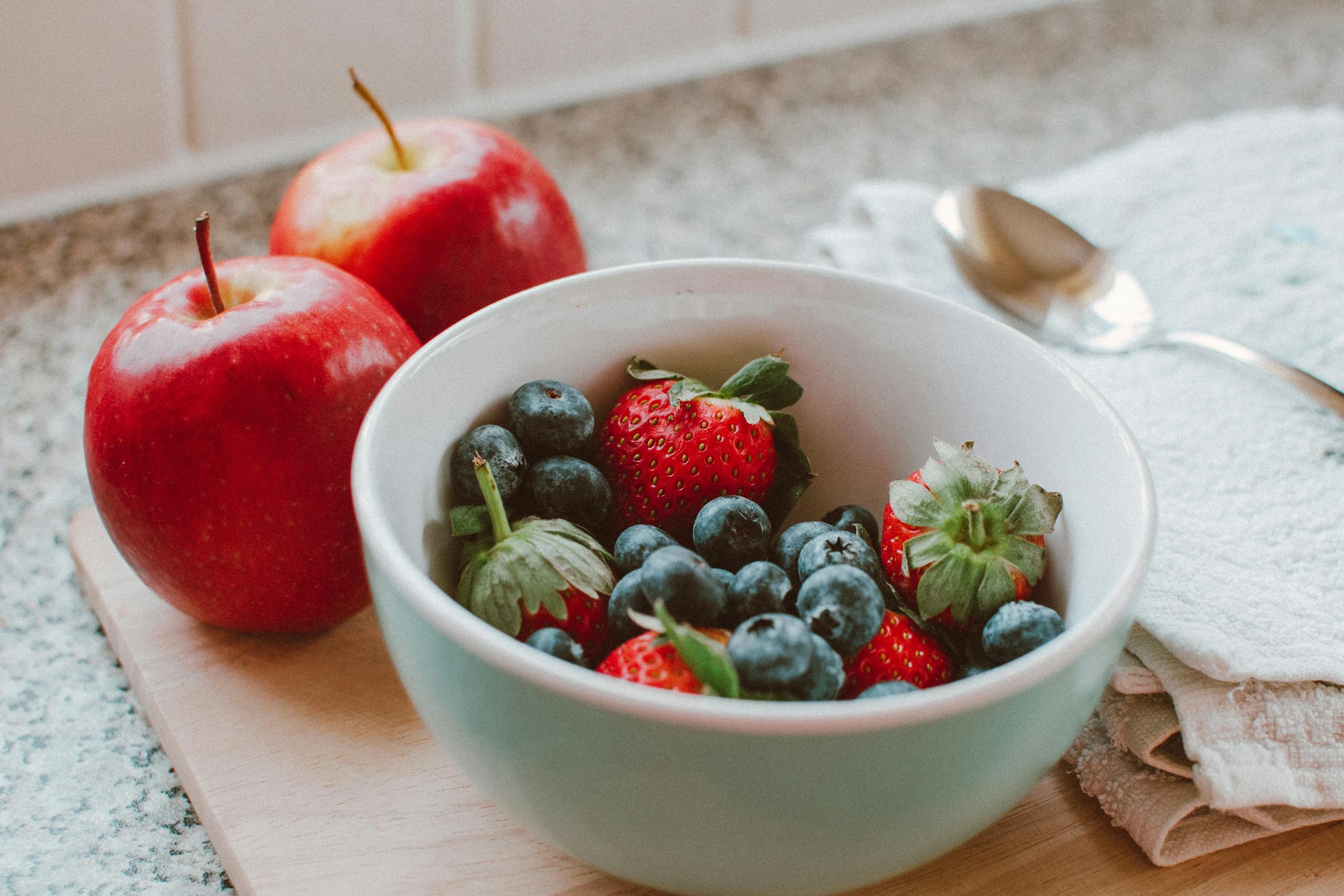 A bowl of fresh berries and apples arranged on a wooden board, perfect for a healthy breakfast.